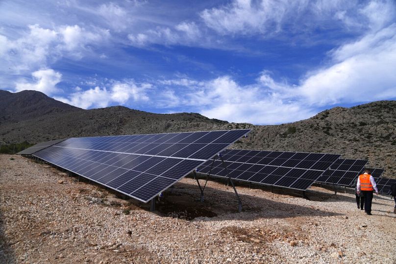 Un homme marche à côté de panneaux solaires dans un parc photovoltaïque sur l'île égéenne de Chalki, novembre 2021