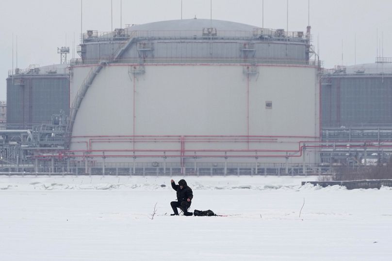 Un homme pêche sur la glace du golfe de Finlande sur fond de réservoirs de stockage de pétrole de Saint-Pétersbourg