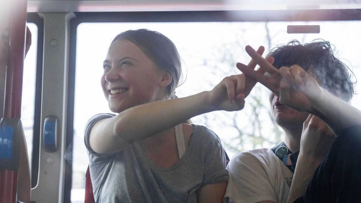 Climate activist Greta Thunberg flashes a V-sign after being detained and driven off in a bus after joining protestors who blocked a road during a climate protest