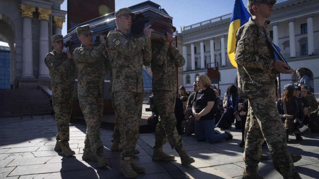 People kneel as soldiers carry the coffins of Ukrainian servicemen during the funeral ceremony in Independence square in Kyiv, Ukraine, Tuesday, April 9, 2024.