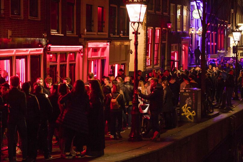 En ce vendredi 29 mars 2019, image d'archives des touristes se baignant dans une lueur rouge émanant des vitrines et des néons des peep shows, dans le quartier rouge d'Amsterdam.