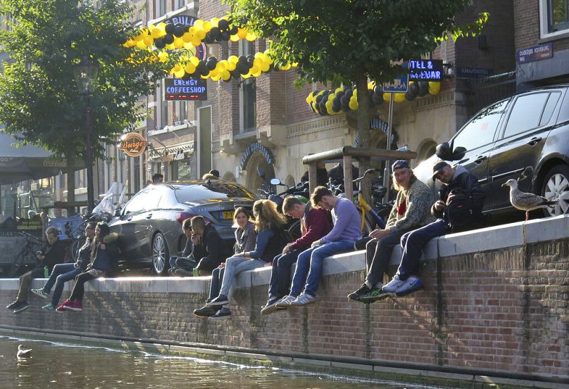 Des touristes sont assis sur le quai d’un canal, devant un café du centre d’Amsterdam, en octobre 2016.