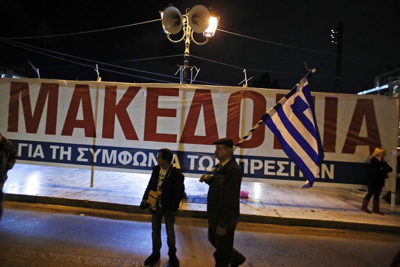 Un opposant à l'accord de Prespa brandit un drapeau grec, debout devant une affiche lors d'un rassemblement devant le Parlement grec, janvier 2019.