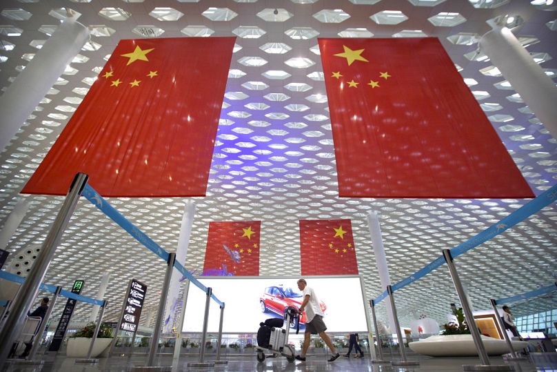 Un voyageur pousse ses bagages sous de grands drapeaux chinois suspendus au plafond de l'aéroport international de Shenzhen Bao'an à Shenzhen, en octobre 2018.