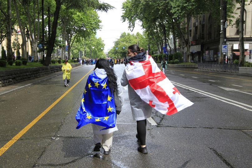 Deux manifestants drapés de drapeaux nationaux géorgiens et de l'UE se dirigent vers le bâtiment du Parlement lors d'une manifestation contre 