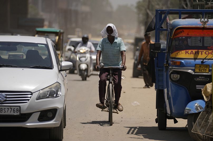 Un homme se couvre le visage d'un tissu pour se protéger de la chaleur alors qu'il roule à vélo dans une rue animée de Jammu, en Inde.