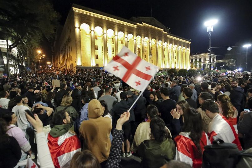 Des manifestants brandissent un drapeau national géorgien alors qu'ils se rassemblent devant le bâtiment du Parlement à Tbilissi.