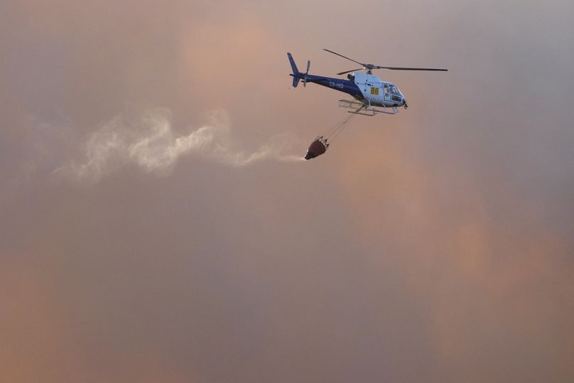 Un hélicoptère de lutte contre les incendies vole au milieu des nuages ​​de fumée provenant d'un incendie de forêt brûlant près des maisons d'Alcabideche, à l'extérieur de Lisbonne, en juillet 2023.
