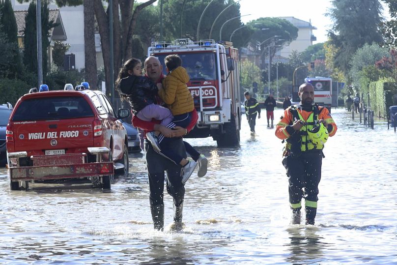 Un homme transporte des enfants dans les eaux de crue, avec des services d'urgence sur place après de fortes pluies, en Toscane, en Italie, en novembre 2023.