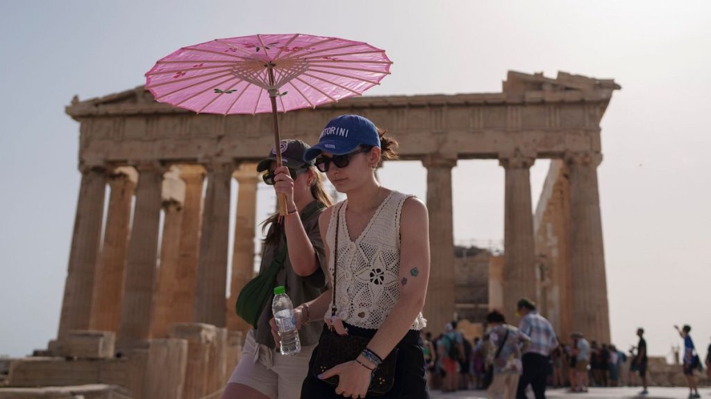 Tourists with an umbrella walk in front of the Parthenon at the ancient Acropolis in central Athens, 12 June 2024.