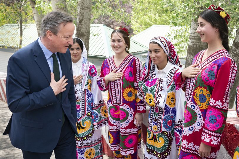 Le ministre britannique des Affaires étrangères, David Cameron, est accueilli par des femmes en costumes traditionnels lors de sa visite au projet hydroélectrique de Nurek, à environ 70 km au sud de Douchanbé, le 22 avril 2024.