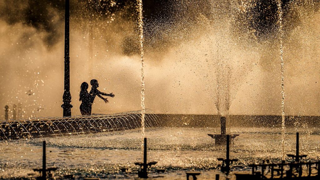 Children enjoy the drizzle from a public fountain before sunset in Bucharest, Romania, Thursday, June 20, 2024