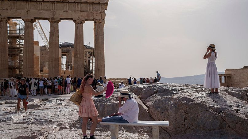 Un touriste utilise un éventail pour en rafraîchir un autre assis sur un banc devant le Parthénon de l'ancienne Acropole, à Athènes, le 12 juin 2024. 