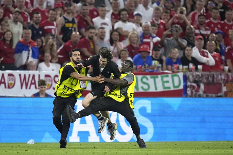 Des agents de sécurité s'attaquent à un homme qui court sur le terrain lors d'un match du groupe C entre le Danemark et la Serbie lors du tournoi de football Euro 2024 à Munich, en Allemagne, le mardi 25 juin 2024.
