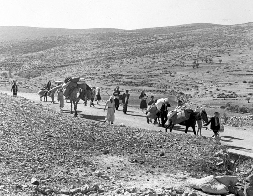 Un groupe de réfugiés palestiniens marchent le long de la route poussiéreuse reliant Jérusalem au Liban, transportant avec eux leurs enfants et leurs affaires, novembre 1948.