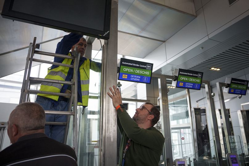 Les employés de l'aéroport installent un panneau d'information à côté des portes automatiques de contrôle des frontières non Schengen, à l'aéroport international Henri Coanda, près de Bucarest, mars 2024.