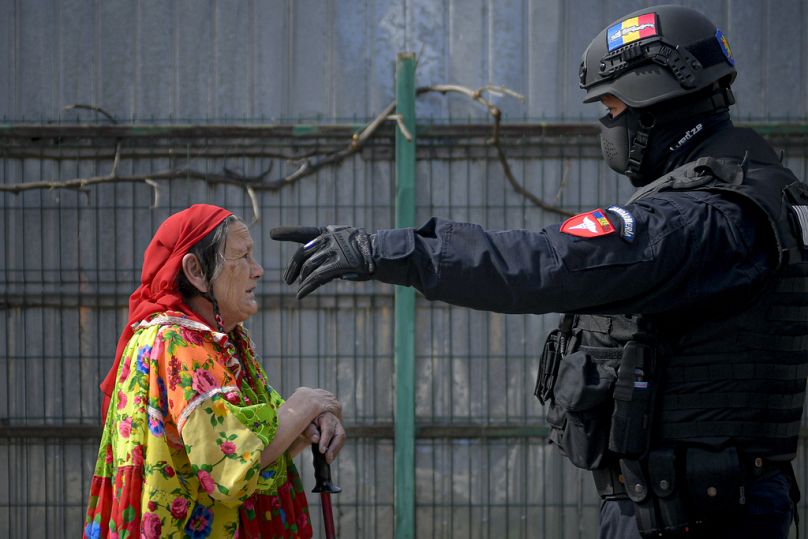 Un policier anti-émeute fait un geste en essayant de refouler une vieille femme rom roumaine lors d'un raid de la Garde nationale de l'environnement à Vidra, le 13 avril 2021.