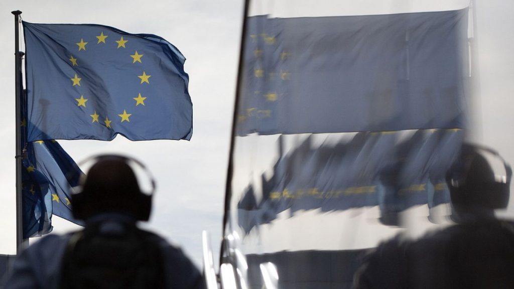 A man wearing headphones walks toward EU flags as he is reflected in the marble of the European Commission building in Brussels, 19 August 2020