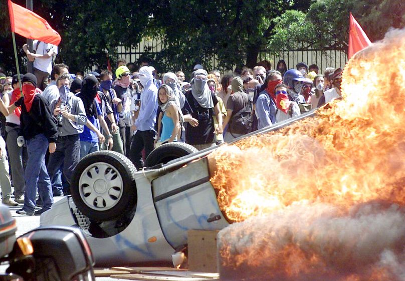 Des manifestants masqués passent devant une voiture en feu lors d'affrontements entre militants altermondialistes et policiers anti-émeutes à Gênes, Italie, 2001.