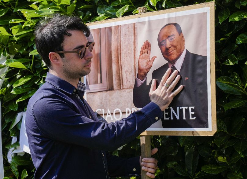 Un homme pose à côté d'une affiche de Silvio Berlusconi devant la résidence de ce dernier à Arcore, près de Milan, le 12 juin 2023