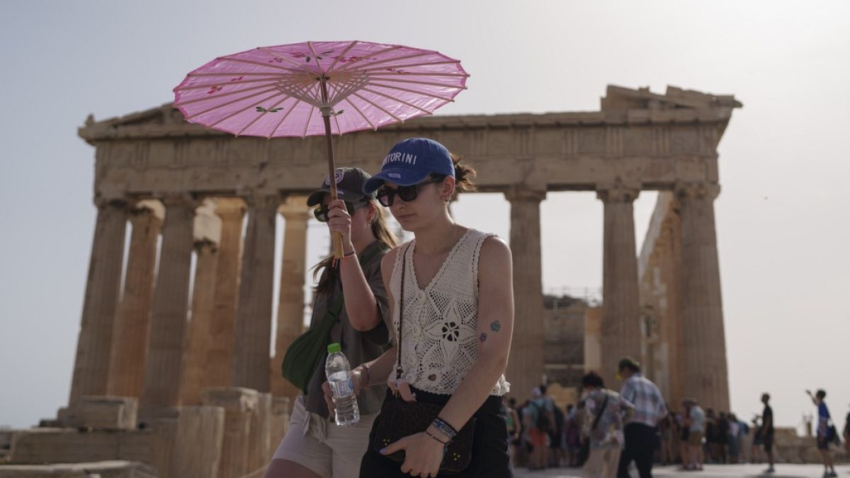 Tourists with an umbrella walk in front of the Parthenon at the ancient Acropolis in central Athens, June 12, 2024.