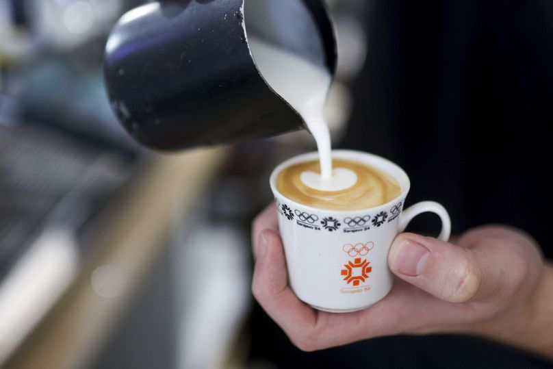 Un barman verse du lait dans une tasse à café conçue pour les Jeux olympiques de Sarajevo dans un café Kawa du centre-ville de Sarajevo, le 5 février 2024