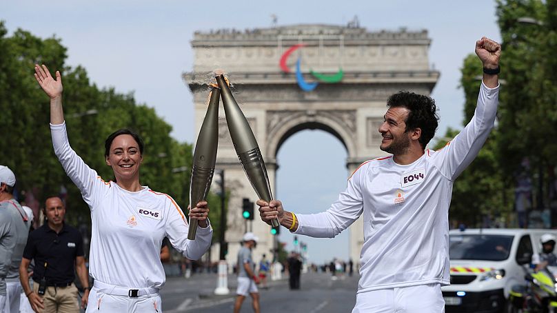 Nina Metayer, pâtissière française, et le chanteur franco-israélien Amir portent la torche olympique sur l'avenue des Champs-Elysées, avec l'Arc de Triomphe en arrière-plan