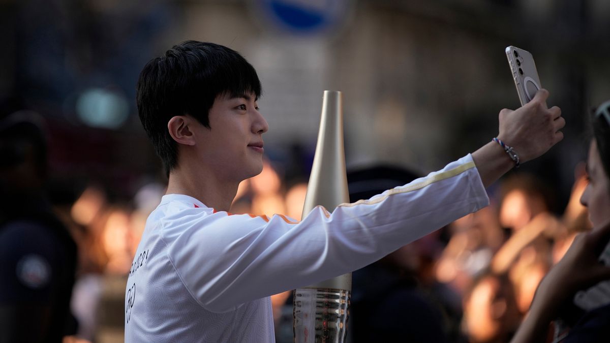 Jin, the oldest member of K-pop supergroup BTS, males a selfie with the Olympic torch, Sunday, July 14, 2024 in Paris.