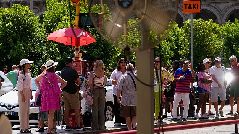 Des touristes attendent un bus sous le soleil à Milan, en Italie, le mardi 16 juillet 2024.