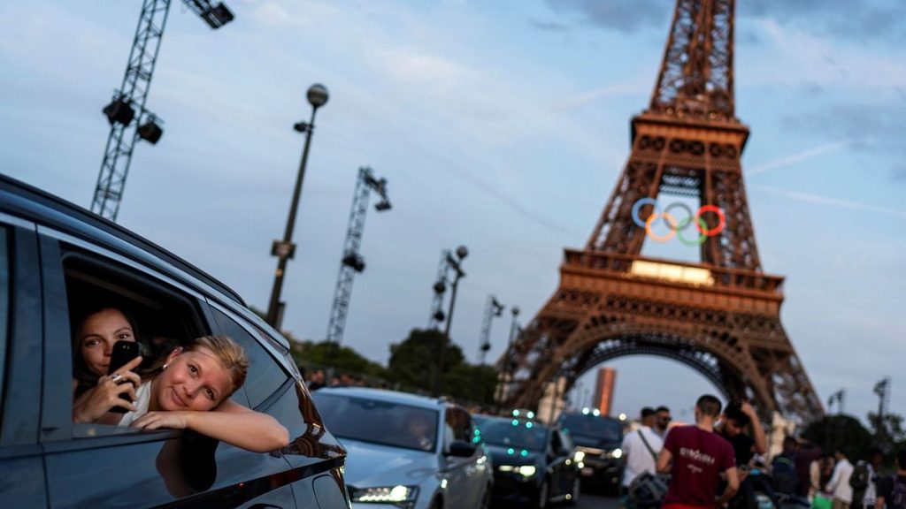 Passengers in the back of a taxi film themselves as they leave the Eiffel Tower decorated with the Olympic rings ahead of the 2024 Summer Olympics, 17 July 2024.
