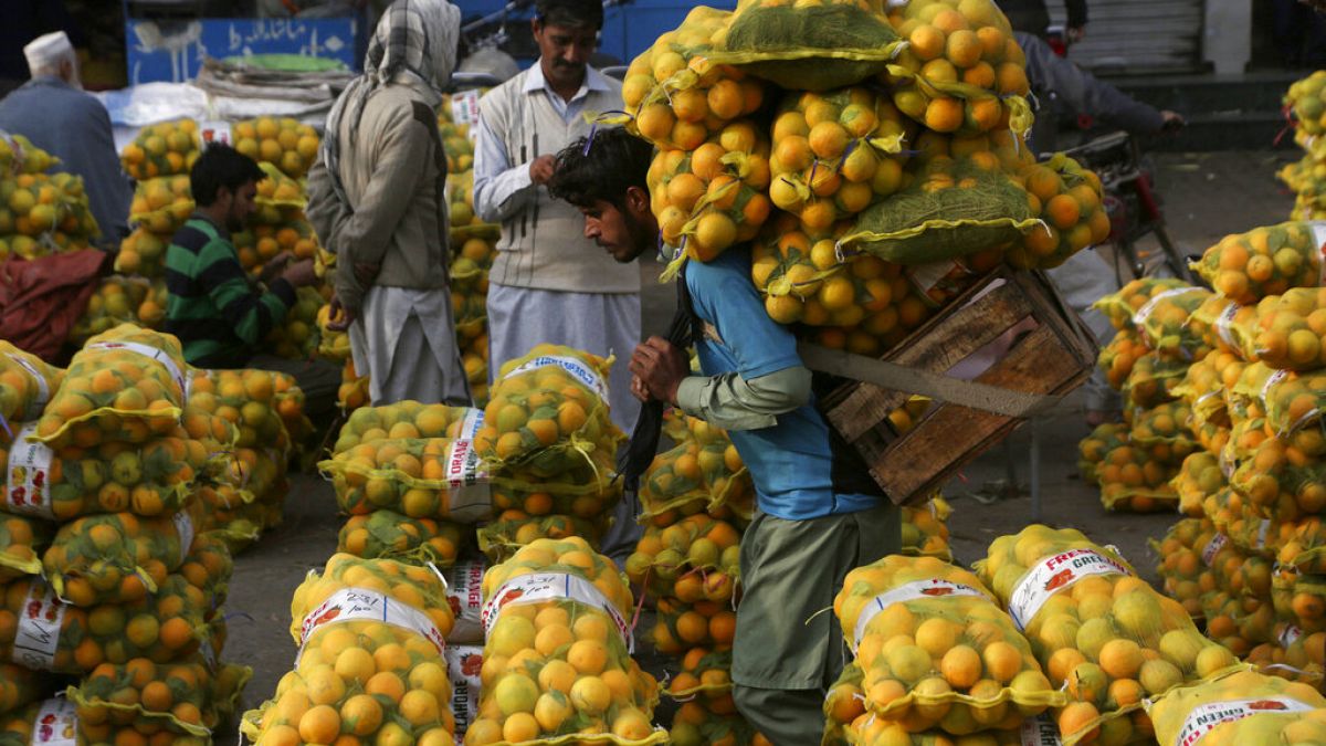 A laborer carries sacks of oranges in a wholesale fruit market in Lahore, Pakistan, on Dec. 1, 2021...