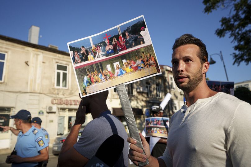 Tristan Tate tient une photo d'une scène qui a eu lieu lors de la cérémonie d'ouverture des Jeux olympiques de Paris et qui semble évoquer l'œuvre de Léonard de Vinci. "Le dernier souper," pendant une manifestation