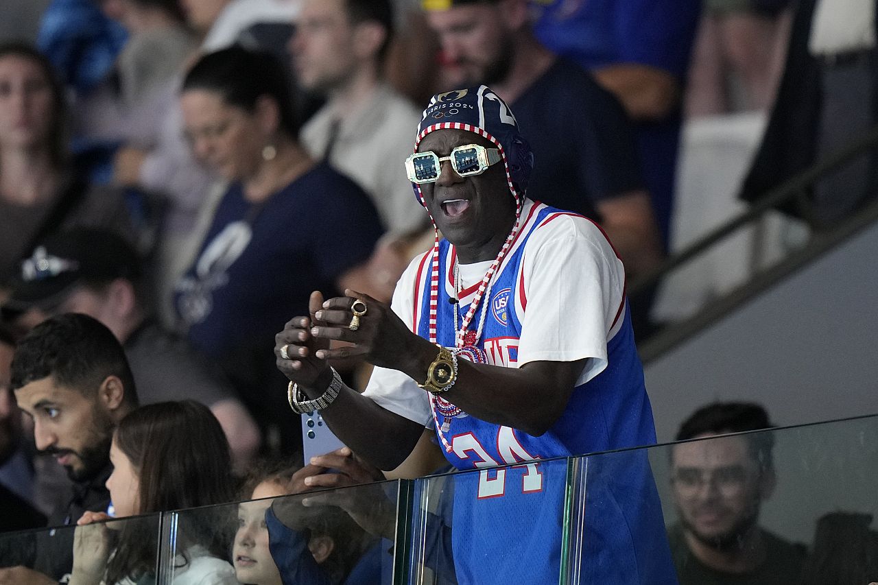 Le légendaire rappeur américain Flavor Flav célèbre après un match préliminaire du groupe B de water-polo féminin entre les États-Unis et la Grèce aux Jeux olympiques d'été de 2024