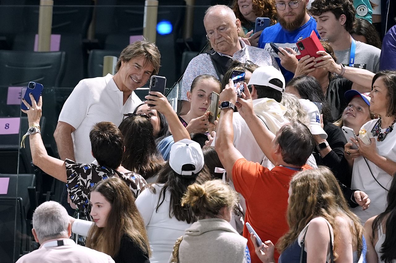 L'acteur Tom Cruise, à gauche en blanc, pose pour des photos avec des fans alors qu'il assiste au tour de qualification de gymnastique artistique féminine aux Jeux olympiques d'été de 2024