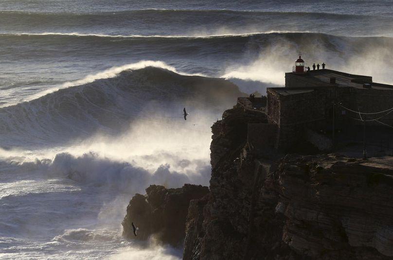 Les gens au sommet du phare de Nazaré regardent les vagues se briser lors d'une séance de surf sur de grosses vagues à Praia do Norte, ou plage du Nord, à Nazaré, en février 2017