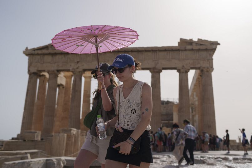 Des touristes avec un parapluie se promènent devant le Parthénon de l'ancienne Acropole dans le centre d'Athènes, en juin 2024
