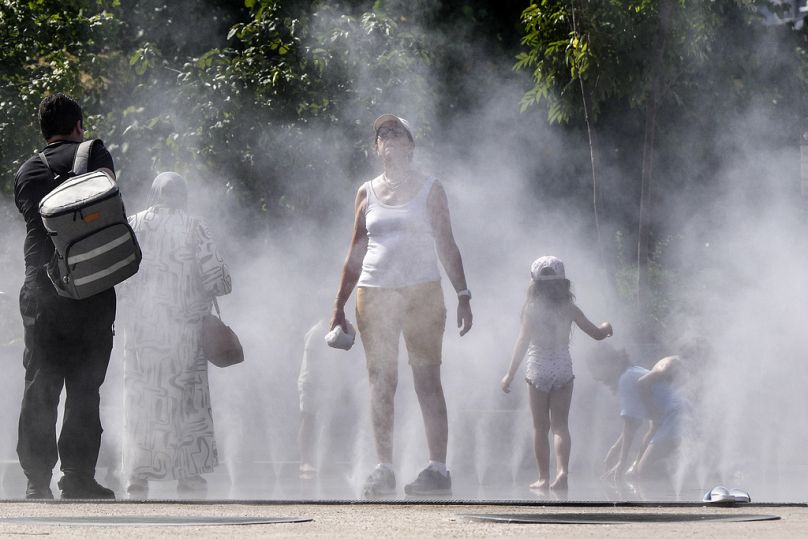 Les gens se rafraîchissent sous une douche publique à brouillard d'eau dans le centre de Paris, en France, lors de la cérémonie d'ouverture des Jeux olympiques d'été de 2024, le mardi 30 juillet 2024