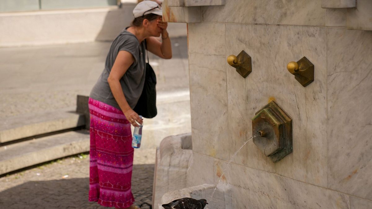 A woman cools herself as a pigeon drinks water from a public fountain in Belgrade, Serbia, 21 June 2024.