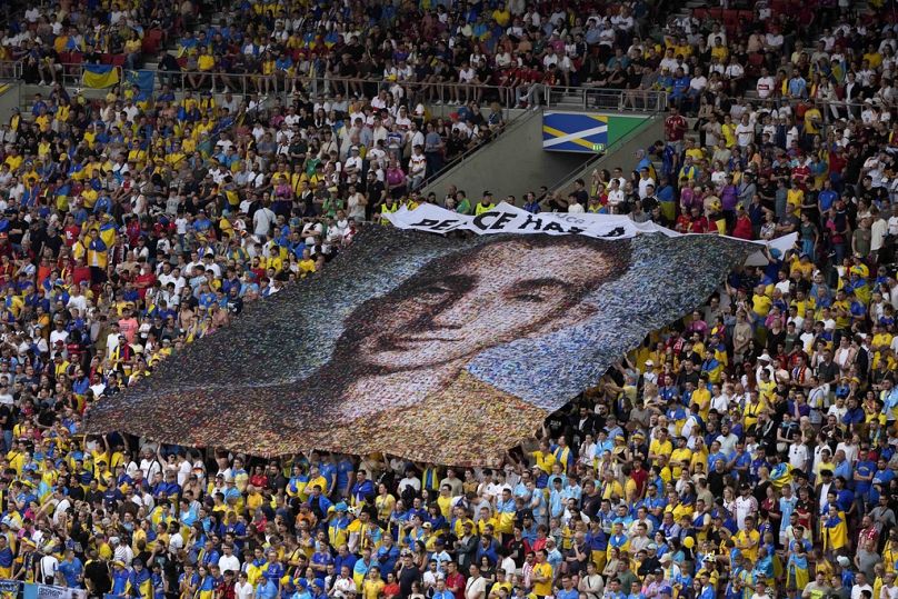 Des supporters ukrainiens arborent une banderole sur laquelle on peut lire « La paix a un prix » et un portrait de Nazariy Hryntsevich, un soldat tombé au combat et un fan de football, lors du match entre l'Ukraine et la Belgique