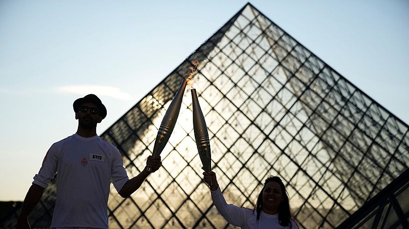 Le photographe français JR, à gauche, et l'athlète Sandra Laoura tiennent la torche olympique dans la cour du musée du Louvre, le 14 juillet 2024 à Paris.