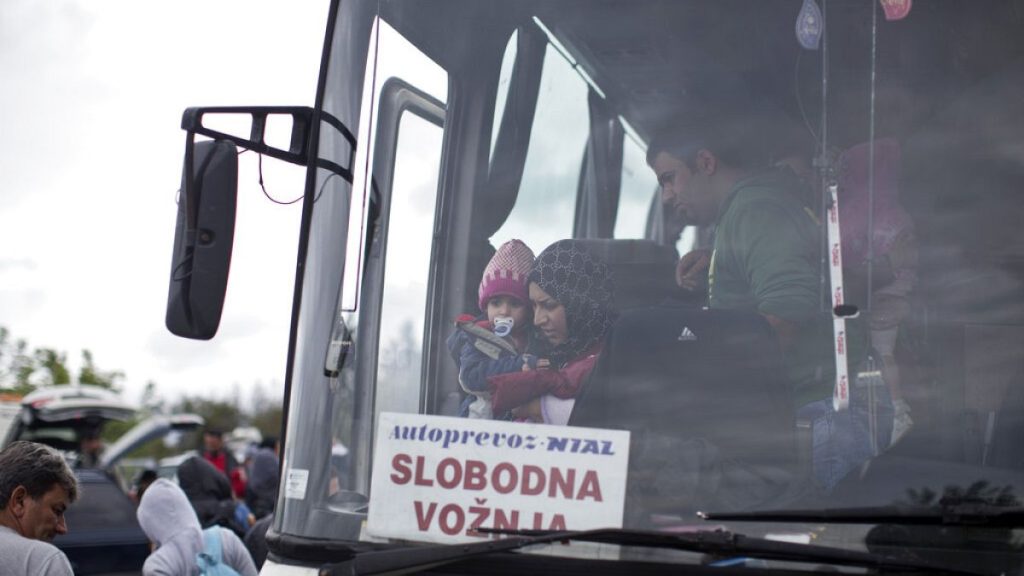 A woman carries a child as she exits a bus that transported her to Serbia