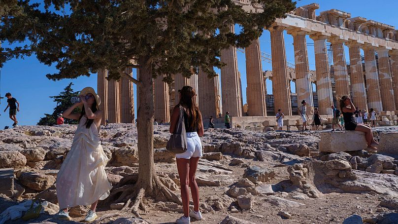 Une femme boit de l'eau devant l'ancien temple du Parthénon lors d'une journée chaude et venteuse sur la colline de l'Acropole, à Athènes, le mardi 16 juillet 2024. 