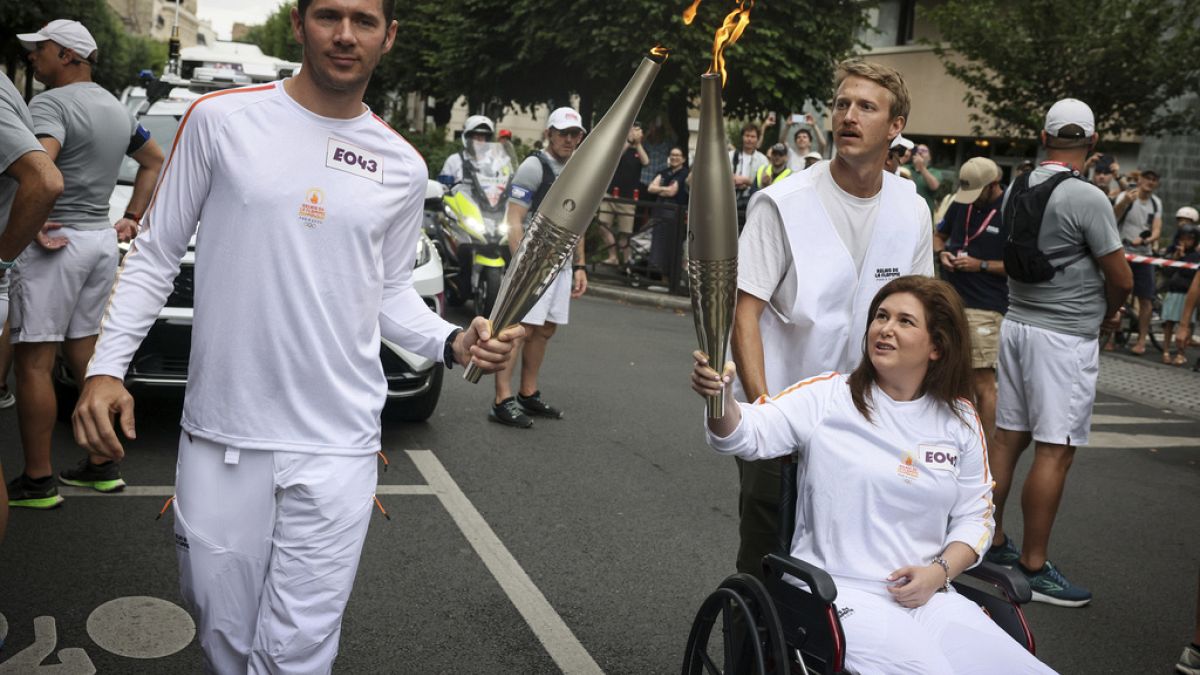 Press agency photographer Christina Assi, right, holds the Olympic torch with. Nicolas Payeur, left, at the 2024 Summer Olympics, Sunday, July 21, 2024,