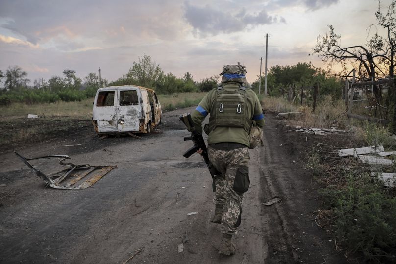 Sur cette photo fournie par le service de presse de la 24e brigade mécanisée d'Ukraine, un militaire de la 24e brigade mécanisée passe devant une voiture endommagée dans la ville de Chasiv, en première ligne.