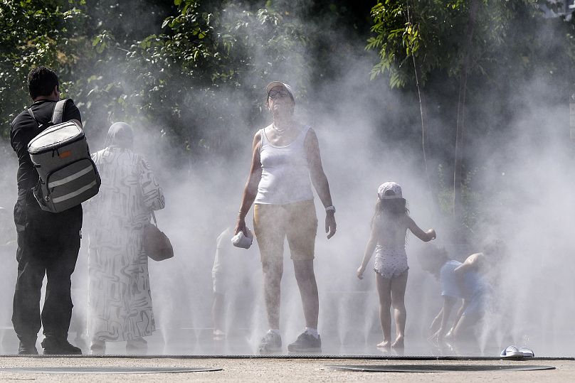 Les gens se rafraîchissent dans une douche publique à brouillard d'eau dans le centre de Paris, en France.