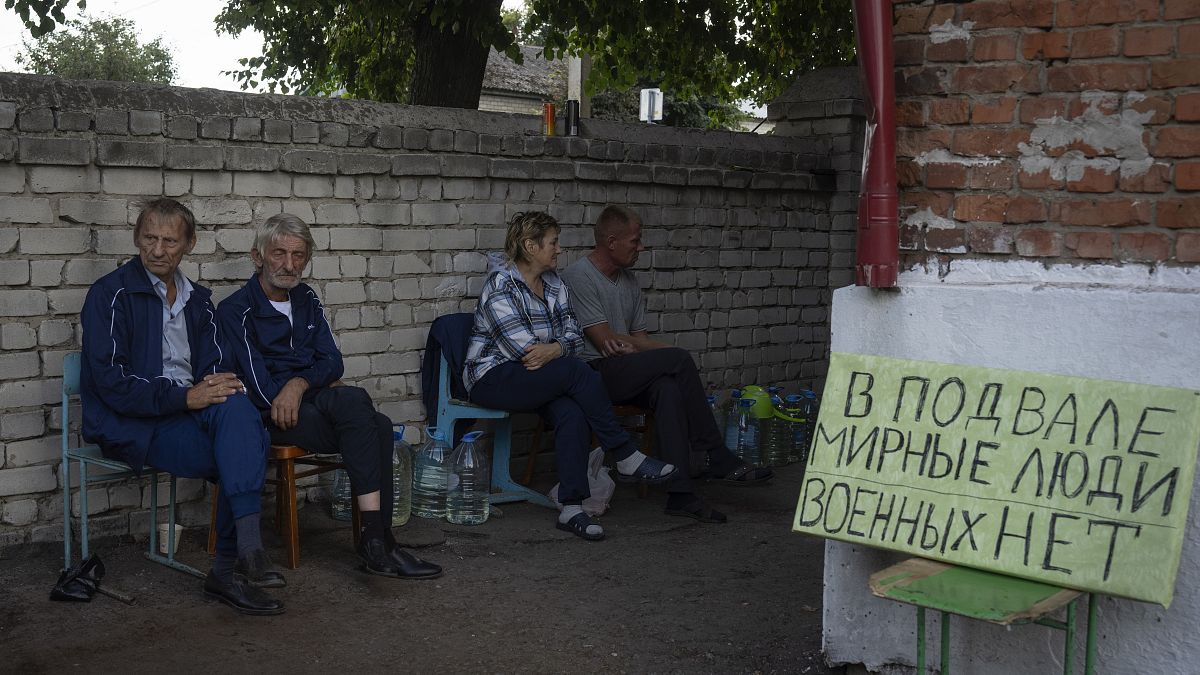 Local residents sit near a shelter in Sudzha with a sign that reads