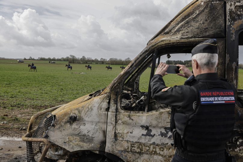 Un policier prend une photo avec son téléphone portable alors qu'il se tient à côté de véhicules de police incendiés après des affrontements avec des manifestants à Sainte-Soline, dans l'ouest de la France, en mars 2023