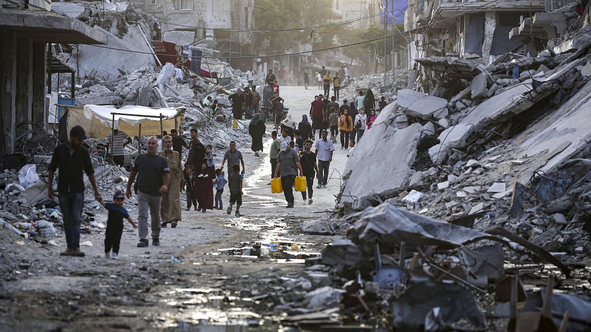 FILE - Palestinians displaced by the Israeli air and ground offensive on the Gaza Strip, walk through a dark streak of sewage flowing into the streets.