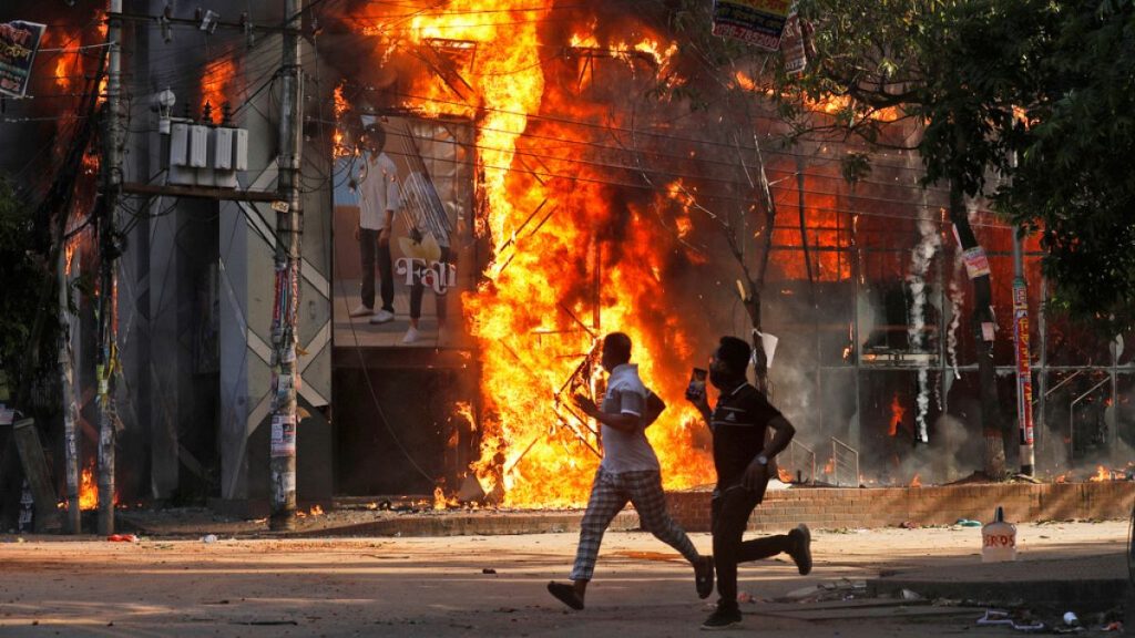 Men run past a shopping center which was set on fire by protesters during a rally against Prime Minister Sheikh Hasina and her government.