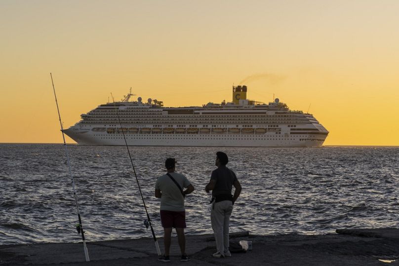 Des pêcheurs regardent un bateau de croisière quitter le port de Montevideo, mars 2024